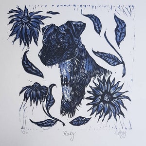 Peut inclure: Une estampe linogravure bleue et blanche d'un chien nommé "Ruby" entouré de fleurs et de feuilles stylisées. L'estampe est numérotée 1/20 et signée "E. Begg".