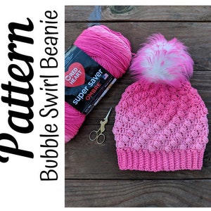 May include: A pink ombre crochet beanie with a white pom pom. The yarn is Red Heart Super Saver Ombre.
