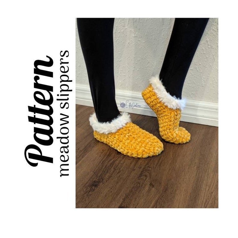May include: Mustard yellow crochet slippers with a fluffy white trim. The slippers are labeled "Pattern meadow slippers" in a stylized font. The slippers are shown on a person wearing black leggings.