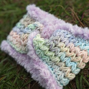 May include: A crocheted headband with a rainbow ombre pattern and a soft, fluffy purple trim.