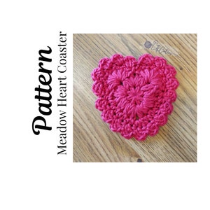 May include: A pink crocheted heart-shaped coaster with a textured design. The coaster is made with a single crochet stitch and has a scalloped edge.
