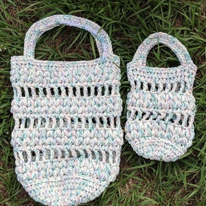 May include: Two crocheted bags made with a white yarn with blue, pink, and purple flecks. The larger bag has a wider opening and a longer handle. The smaller bag has a smaller opening and a shorter handle.