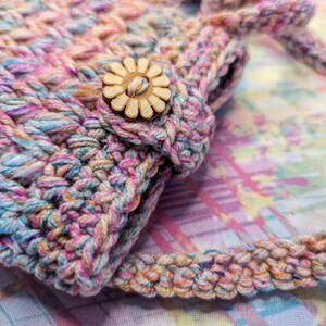 May include: A small crocheted bag with a colorful, multi-colored yarn. The bag has a wooden flower button.