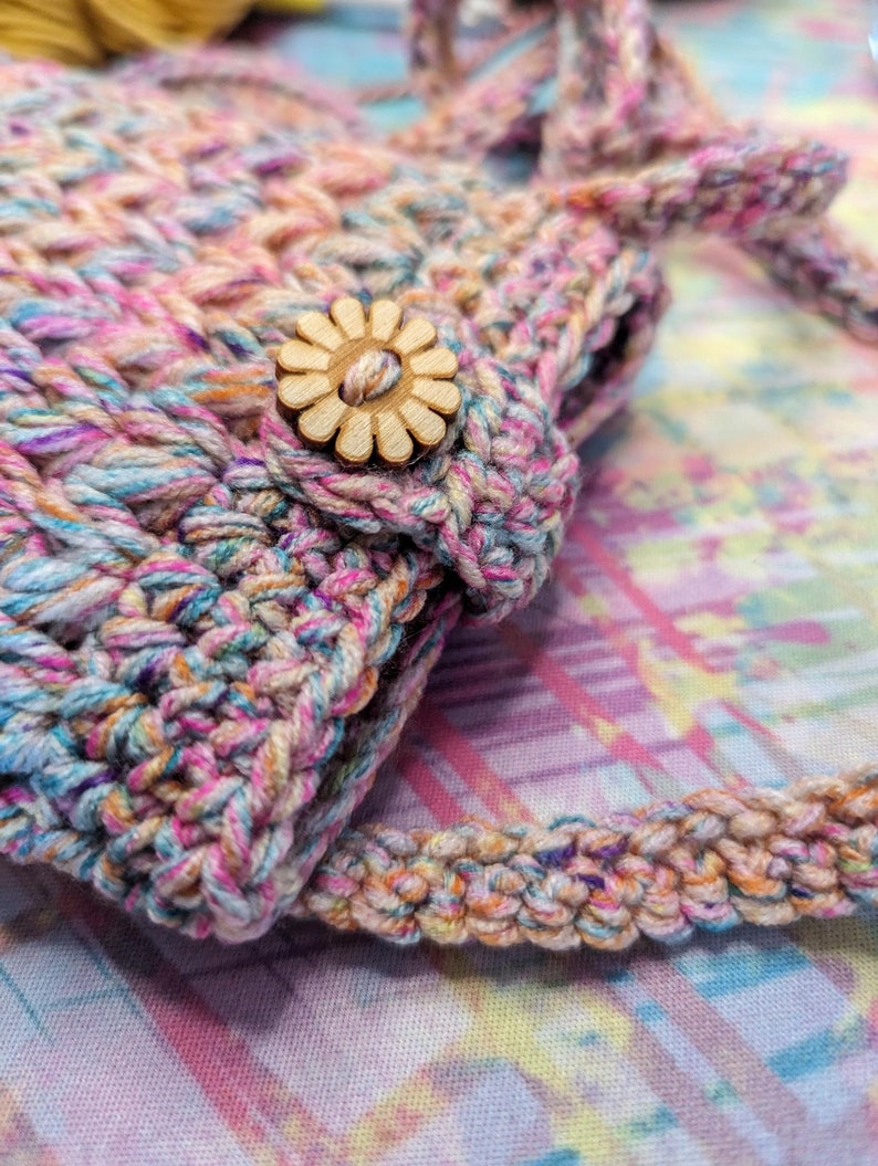 May include: A small crocheted bag with a colorful, multi-colored yarn. The bag has a wooden flower button.