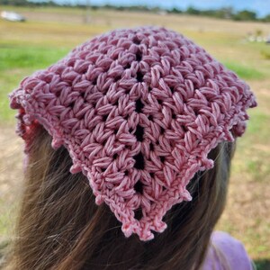 K&ouml;nnte beinhalten: Ein rosa geh&auml;keltes Bandana mit einem gewellten Rand. Das Bandana ist um den Kopf einer Person mit langen braunen Haaren gebunden.