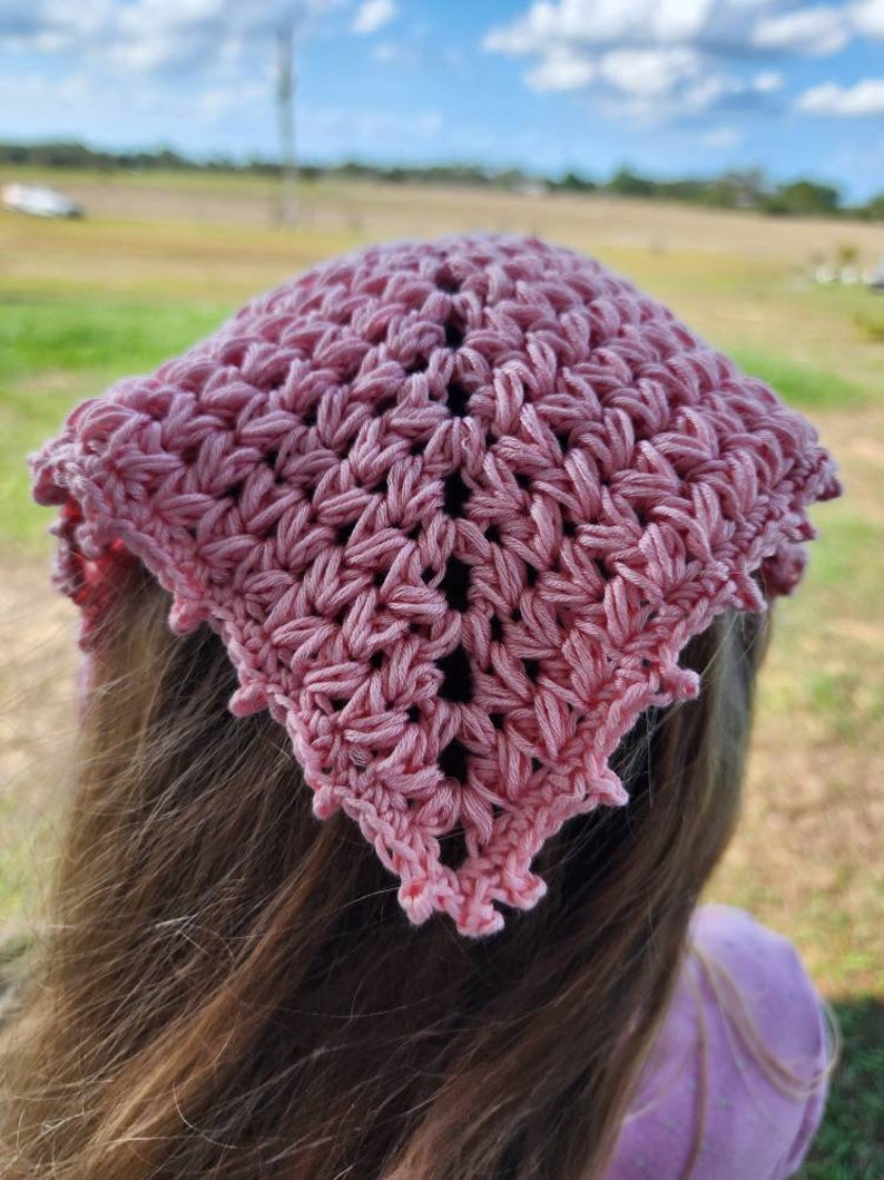 K&ouml;nnte beinhalten: Ein rosa geh&auml;keltes Bandana mit einem gewellten Rand. Das Bandana ist um den Kopf einer Person mit langen braunen Haaren gebunden.