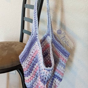 May include: A crocheted tote bag with a purple, pink, and white striped pattern. The bag is hanging on a black chair.