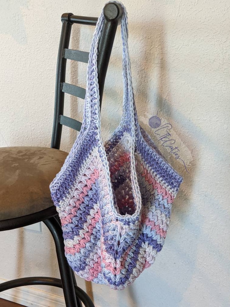 May include: A crocheted tote bag with a purple, pink, and white striped pattern. The bag is hanging on a black chair.