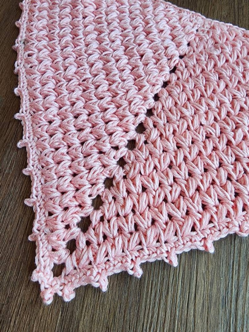 K&ouml;nnte beinhalten: Eine rosa geh&auml;kelte Deckchen mit einem gewellten Rand. Die Deckchen ist mit einem zarten Stichmuster gearbeitet und hat eine Spitzenoptik.