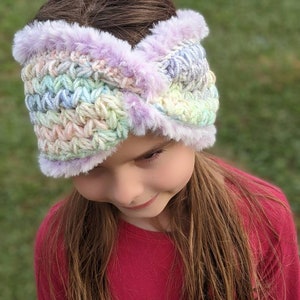 May include: A pastel-colored crochet headband with a purple faux fur trim. The headband is worn by a young person with long brown hair.