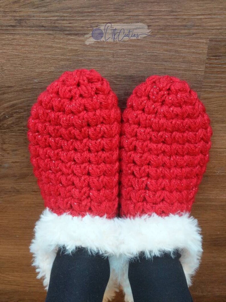 May include: A pair of red crocheted mittens with a white faux fur trim. The mittens are made of a textured yarn and have a sparkly appearance. The mittens are shown on a person wearing black pants.