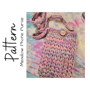 May include: A crocheted phone purse with a colorful, variegated yarn in shades of pink, blue, and cream. The purse has a long strap and a small wooden button with a flower design.