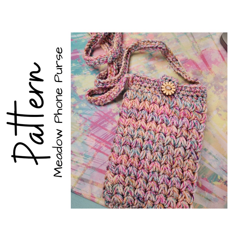 May include: A crocheted phone purse with a colorful, variegated yarn in shades of pink, blue, and cream. The purse has a long strap and a small wooden button with a flower design.
