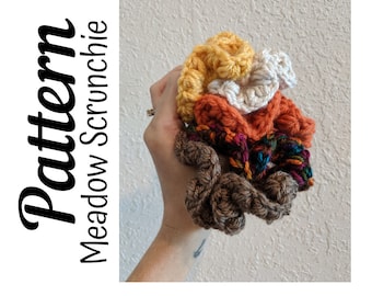 May include: A set of four crocheted hair scrunchies in different colors: brown, orange, cream, and yellow. The scrunchies are stacked on top of each other and are held in a hand. The text "Pattern Meadow Scrunchie" is written vertically on the left side of the image.