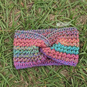 May include: A multi-colored crocheted headband with a twisted knot design. The headband is made with a variety of shades of pink, blue, green, and purple yarn.