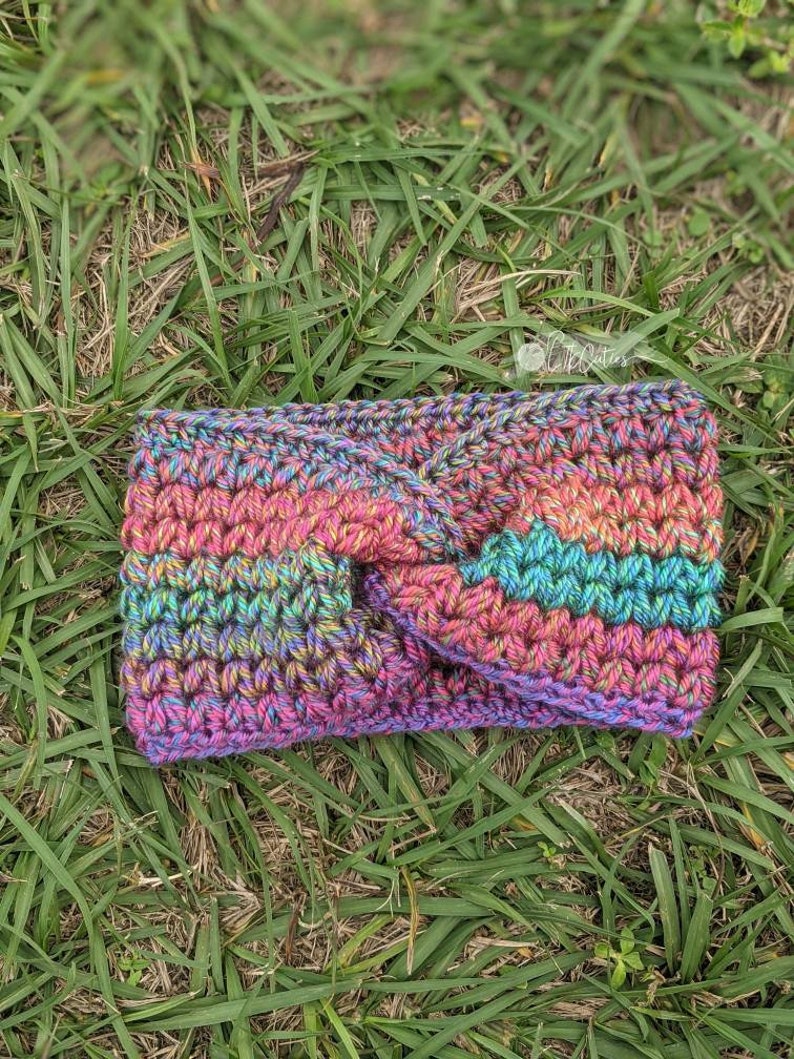 May include: A multi-colored crocheted headband with a twisted knot design. The headband is made with a variety of shades of pink, blue, green, and purple yarn.