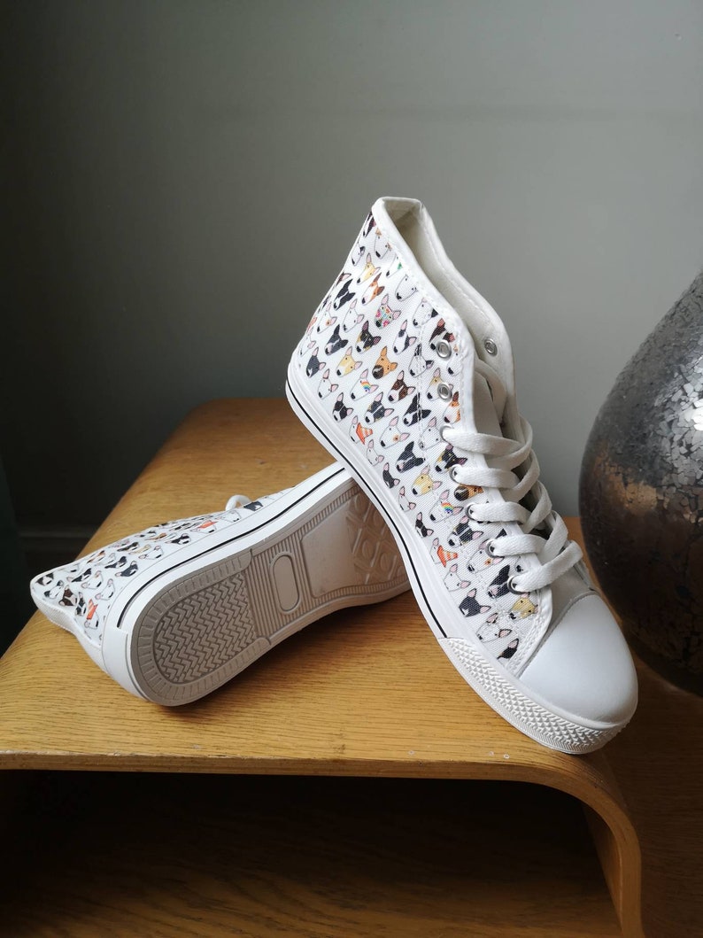 May include: White high-top canvas sneakers with a pattern of colorful bull terrier dog faces.