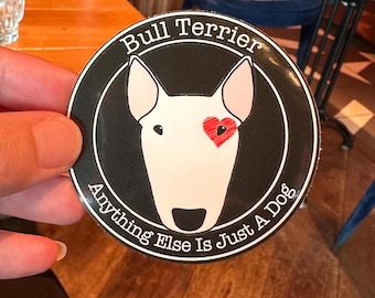 Könnte beinhalten: Ein runder Aufkleber mit einer Bullterrier-Illustration. Der Hund hat ein weißes Gesicht, ein schwarzes Auge und ein rotes Herz über einem Auge. Der Text "Bull Terrier" und "Anything Else Is Just A Dog" sind kreisförmig angeordnet.