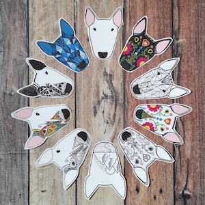 May include: A collection of Bull Terrier head stickers with various designs. Some are white with pink ears, while others feature geometric patterns, floral motifs, and intricate black and white illustrations. The stickers are arranged in a circular pattern.