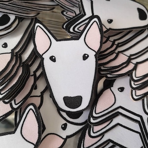 Könnte beinhalten: Ein Stapel weißer Bullterrier-Hundepatchs mit schwarzen Umrissen und rosa Ohren. Die Patches sind aus Stoff und haben ein gesticktes Design.