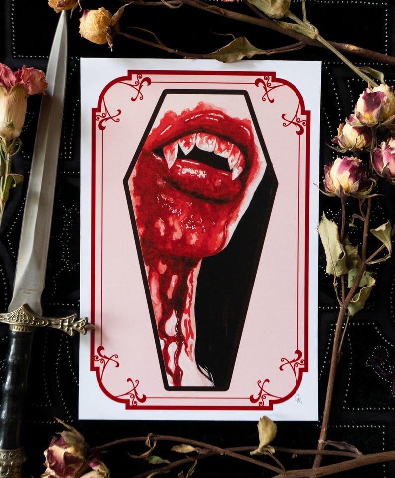 May include: A print featuring a vampire's mouth with sharp fangs, dripping with red blood, inside a coffin-shaped frame. The artwork has a gothic theme, with a red and black color scheme. Dried roses and a decorative dagger are in the background.