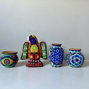 May include: A collection of colorful beaded art pieces, including two small pots, a decorative eagle, and two vases. The pots and vases have wooden rims and intricate patterns in blue, yellow, and green. The eagle is red, yellow, blue, and green.