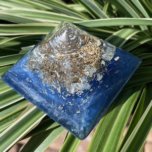 May include: A blue crystal pyramid with gold and silver flakes embedded in the resin. The pyramid has a clear, swirling center.