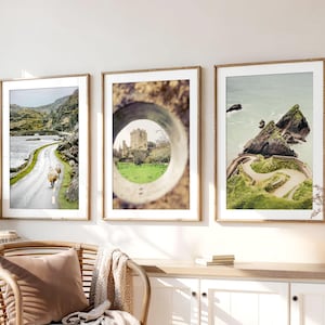 May include: Three framed landscape prints. The first shows a road with sheep, the second a castle framed by a circular opening, and the third a coastal view with a winding path. All are in wooden frames.