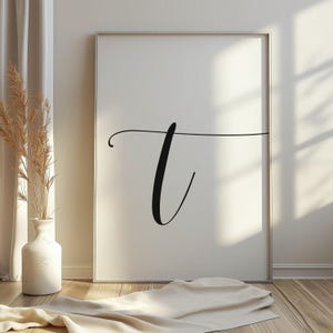 Puede incluir: Una impresión de arte de pared minimalista en blanco y negro con la letra "T" en una fuente cursiva.