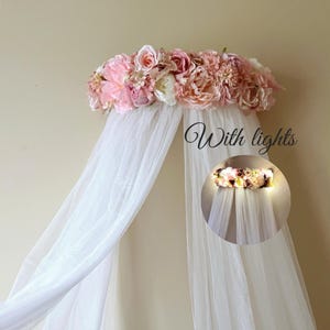Könnte beinhalten: Ein weißes Baldachin mit einem Blumenschmuck aus rosa und weißen Blumen. Der Text "With lights" ist auf dem Bild geschrieben. Das Baldachin ist für das Aufhängen über einem Bett oder einer Wiege konzipiert und schafft eine weiche und romantische Atmosphäre.