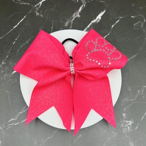 May include: A bright pink cheer bow with a sparkly finish and a rhinestone design in the shape of a heart.