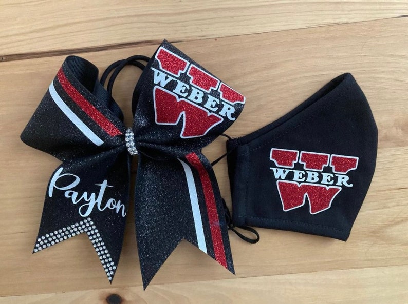 May include: A black glitter cheer bow with red and white accents, the name "Payton" in white script, and a matching face mask. Both items feature the word "WEBER" in red glitter.