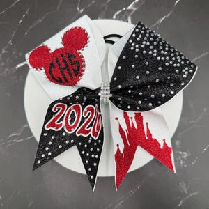 May include: A cheerleading bow with a white base, featuring a red Mickey Mouse head with "CHS" and the year "2020". The bow has black and white sections with rhinestone accents and a rhinestone center.