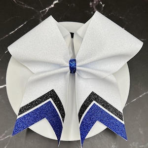 May include: A white glitter cheer bow with a blue glitter accent and black glitter stripes. The bow is centered on a white surface. The bow is a cheerleading accessory.