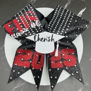 May include: A black glitter hair bow featuring red glitter text that reads FHS class of 2025. A white glitter graduation cap cutout with the name Cherish in black script is centered on the bow, which is embellished with silver rhinestones.