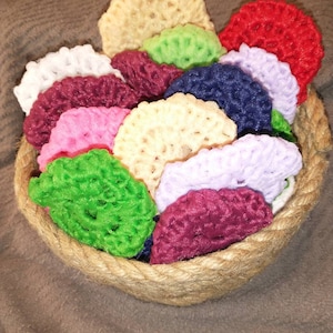 May include: A collection of colorful crocheted coasters in a woven basket. The coasters are in shades of red, pink, purple, green, yellow, and white.