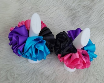 May include: Two sets of colorful hair scrunchies made from ruffled ribbon. The scrunchies are in shades of pink, purple, blue, and black.
