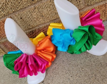 May include: Two white foam mannequin legs with colorful ruffled ribbon tied around them. The ribbon is in the colors of the rainbow, starting with yellow, orange, red, green, blue, and purple.