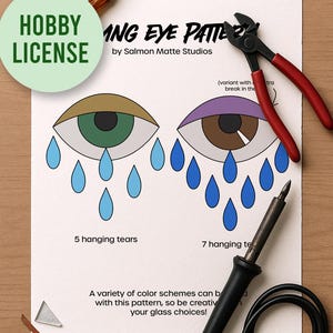 May include: A craft project layout featuring a printed eye pattern with tools. The design includes two stylized eyes with blue teardrops, labeled with text. Tools include pliers, a soldering iron, and a glass cutter. The text reads "HOBBY LICENSE" and "ING EYE PATTERN".