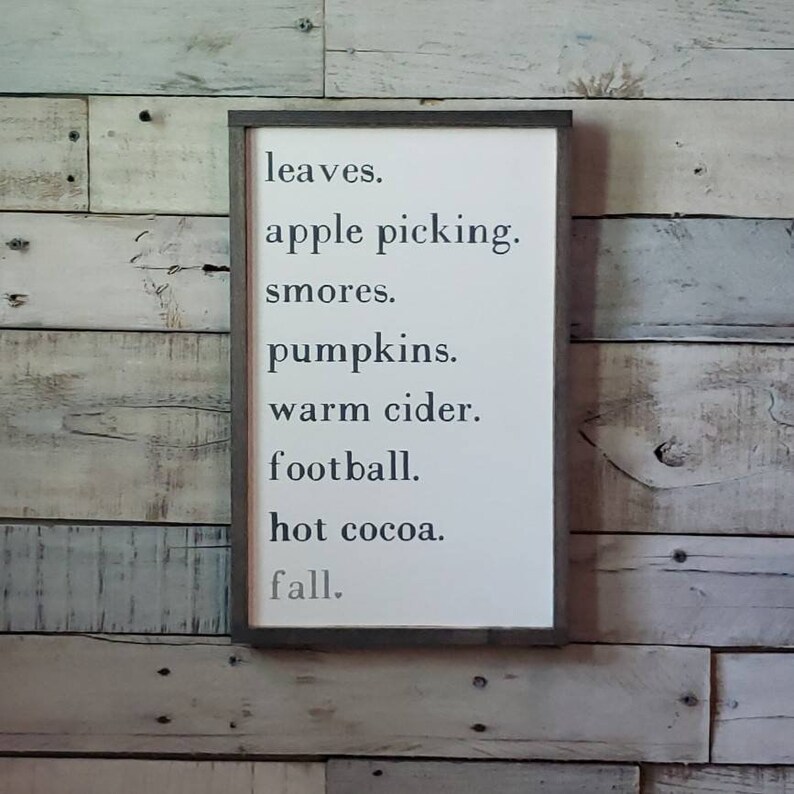 Puede incluir: Un letrero de madera blanco con texto negro que dice "leaves. apple picking. smores. pumpkins. warm cider. football. hot cocoa. fall."