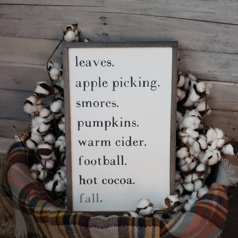 Puede incluir: Un letrero de madera blanco con texto negro que dice "leaves. apple picking. smores. pumpkins. warm cider. football. hot cocoa. fall."