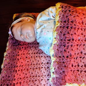 The doll is laying on it's side on a multi-colored striped blanked facing you and the bottom of the blanket covers the bottom of the baby doll.