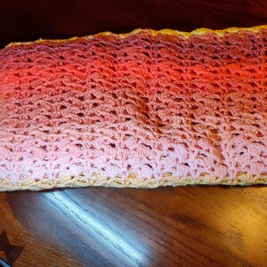 The multi-colored striped blanket if folded up and laying on a wooden table with one corner slightly hanging over the edge.