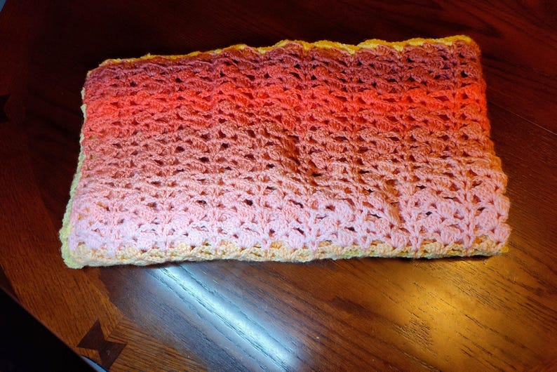 The multi-colored striped blanket if folded up and laying on a wooden table with one corner slightly hanging over the edge.