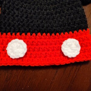A crocheted item featuring a black upper section and a red lower section. The red portion is accented with two circular white crocheted patches positioned side by side, creating a distinct contrast against the vibrant red yarn base.