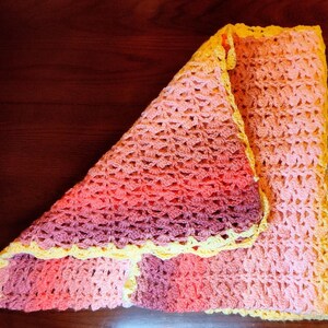 Blanket laying flat on a wooden table folded into a square with the top left  corner folded downward toward the bottom right showing the backside of the blanket.