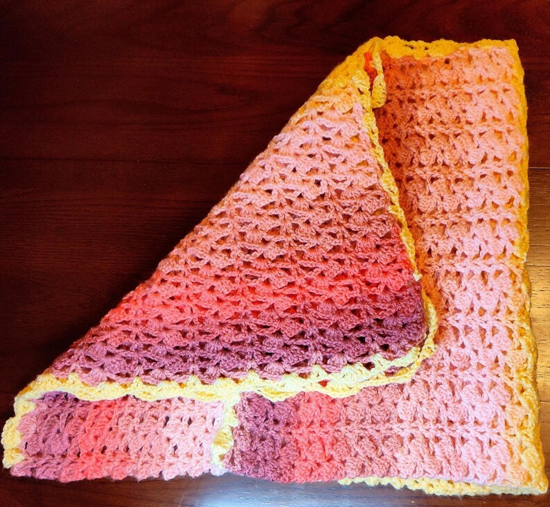 Blanket laying flat on a wooden table folded into a square with the top left  corner folded downward toward the bottom right showing the backside of the blanket.