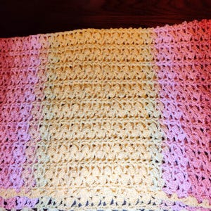 A multi-colored striped blanked is laying on a wooden table and is folded over once in half displaying a center section of yellow and end stripes of pinks, and reds.