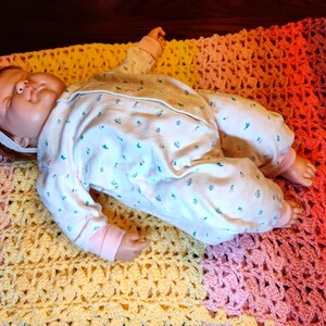 A doll is laying on it's back on top of a fully spread open multi-color striped blanket.