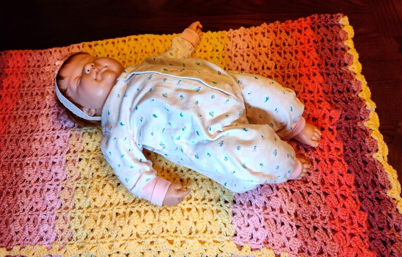 A doll is laying on it's back on top of a fully spread open multi-color striped blanket.